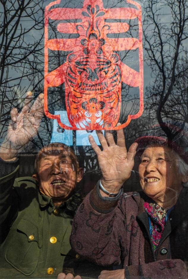 臘月里，霍州市師莊鄉(xiāng)馮南垣村村民師榮光(左)在災(zāi)后重建的新家里貼窗花。(霍州市委宣傳部供圖)