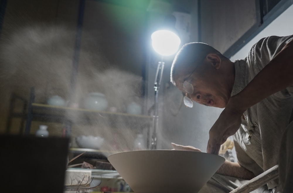 ↑ 在景德鎮(zhèn)，手工匠人吹去坯內(nèi)的泥土（2021年7月14日攝）。