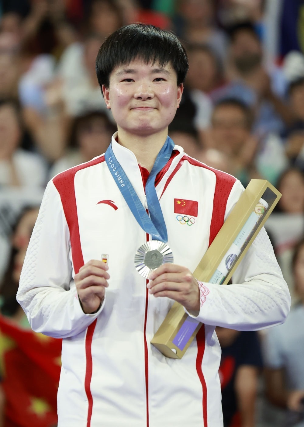 巴黎奧運(yùn)會(huì)羽毛球女子單打亞軍、中國(guó)選手何冰嬌在頒獎(jiǎng)儀式上一手握著銀牌，一手握著西班牙奧委會(huì)徽章（2024年8月5日攝）。新華社記者 任正來(lái) 攝